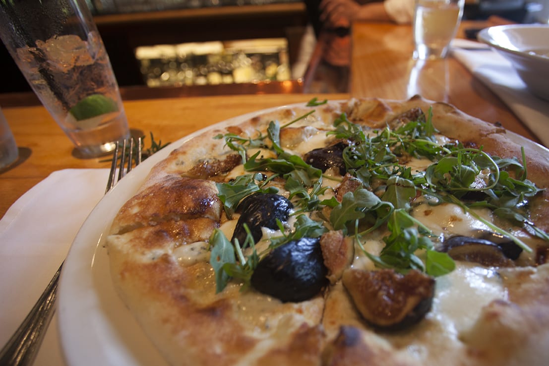 Pizza with figs and arugula on a wooden bar