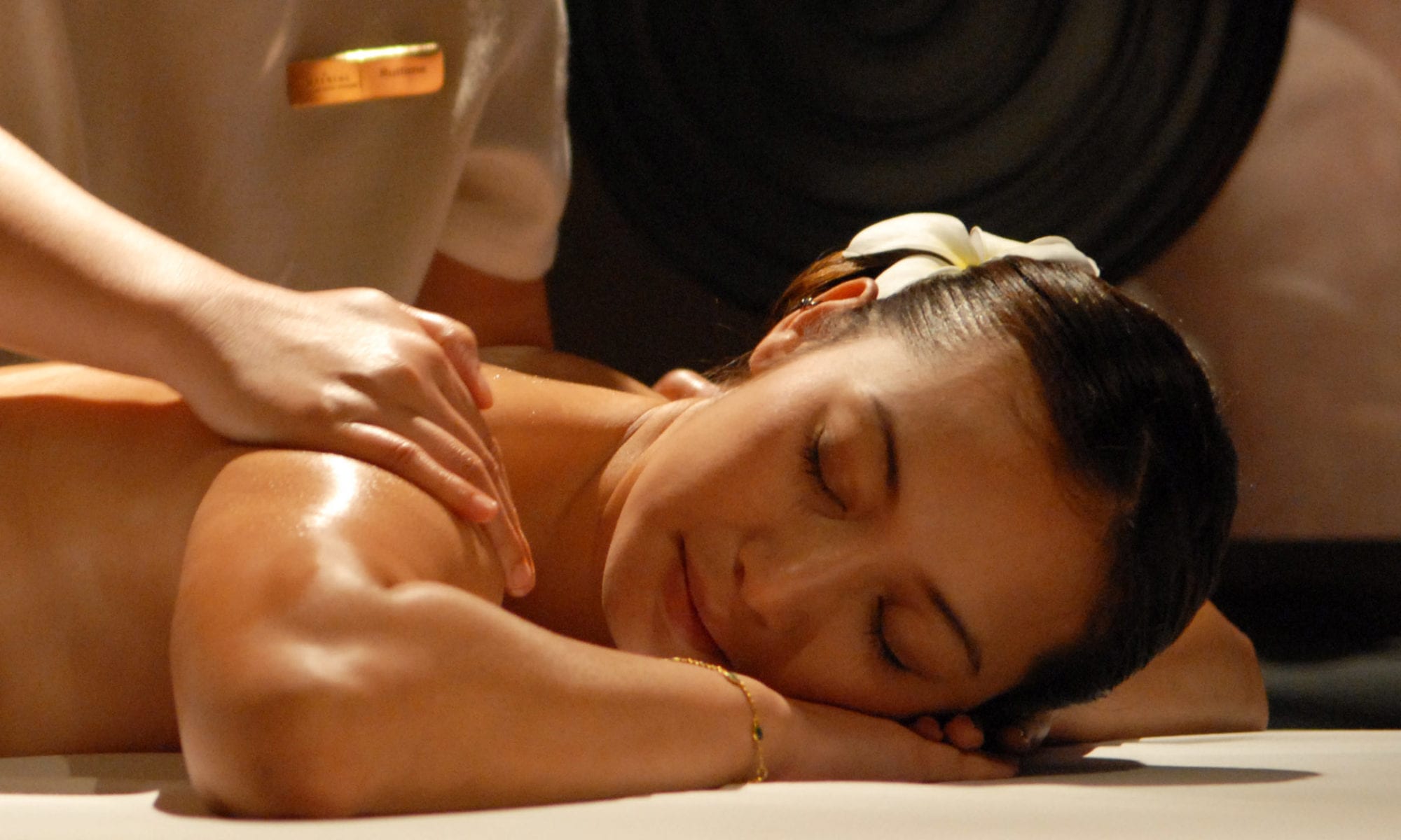 woman laying face-down with a flower in her hair getting a massage